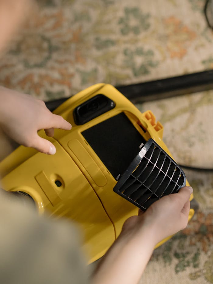 A person is changing the filter of a yellow vacuum cleaner indoors, showing a close-up view.